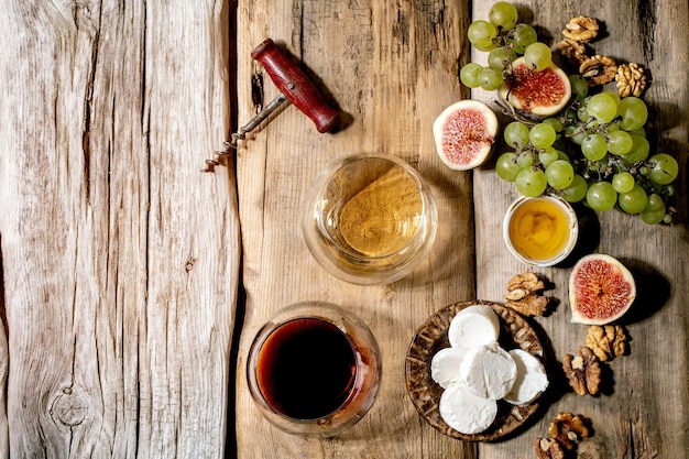 Copas de vino tinto y blanco con uvas, higos, queso de cabra y nueces sobre fondo de madera vieja. Lay Flat, espacio de copia