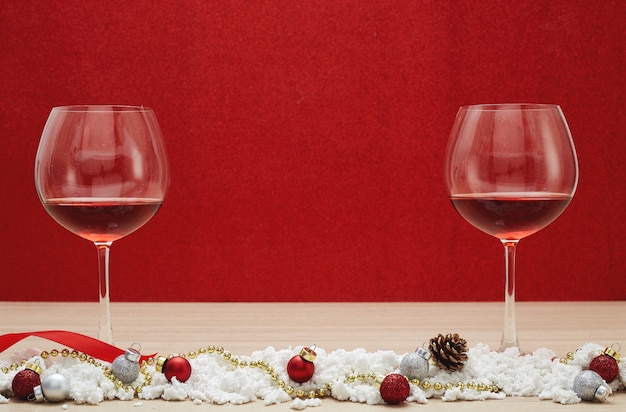 Copas de vino tinto y bolas de navidad en la nieve