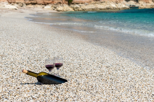 Copas de vino tinto y una botella en la playa en el día soleado de verano