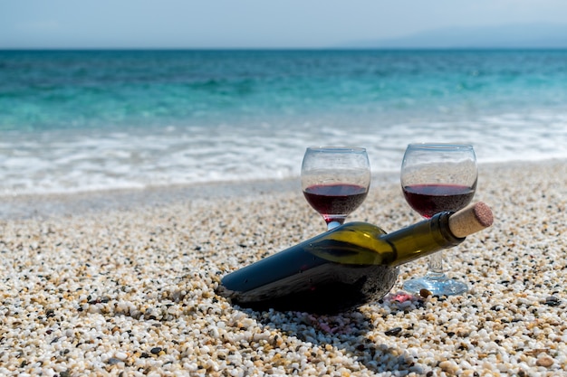 Copas de vino tinto y una botella en la playa en el día soleado de verano