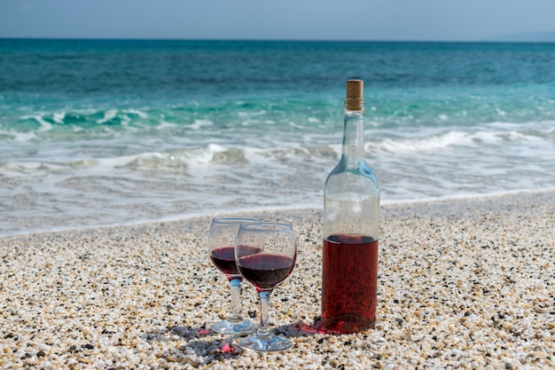 Foto copas de vino tinto y una botella en la playa en el día soleado de verano