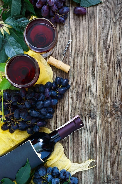 Copas de vino con vino tinto, botella, sacacorchos, uvas azules, hojas sobre una mesa de madera. Fondo de vino con espacio de copia. Vista superior, endecha plana