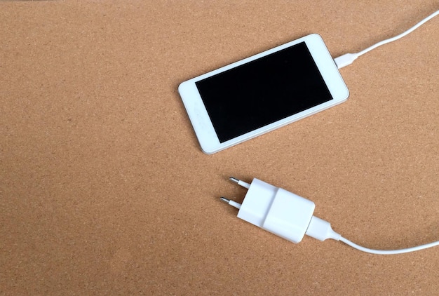 Foto copia el espacio del teléfono inteligente blanco moderno y el cable de carga en fondo marrón