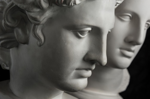 Copia de yeso blanco de la antigua estatua de Apolo y la cabeza de Venus para artistas sobre un fondo de textura oscura. Escultura en yeso del rostro de la estatua.