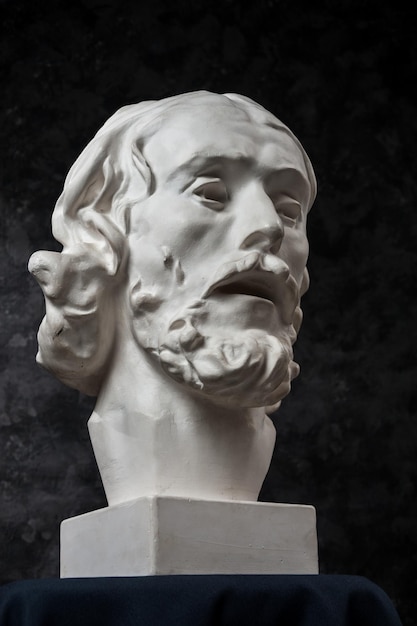 Copia de yeso blanco de la antigua estatua de la cabeza de Juan Bautista para artistas sobre un fondo de textura oscura. Cara de hombre de escultura de yeso. Juan bautizó a Jesús.