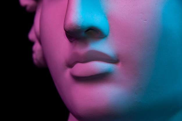 Copia de yeso de colores de la antigua estatua de cabeza humana para artistas sobre un fondo negro. Cerrar vista de labios. Escultura de yeso de rostro humano. Tonos de azul y morado. Cyberpunk, cartel de estilo surrealista.