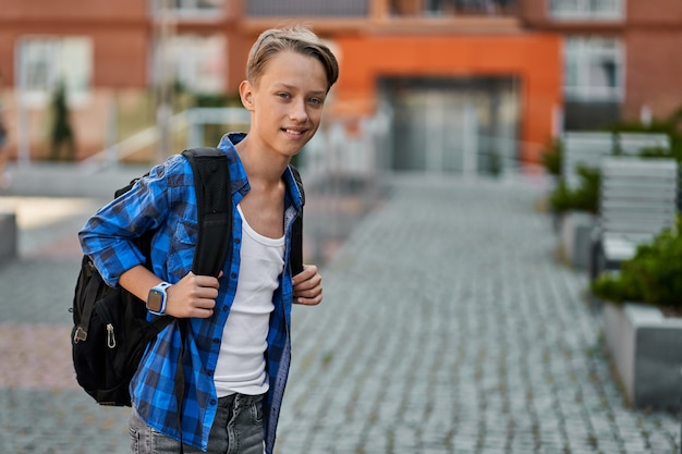 Copiar el retrato de espacio de niño alumno con mochila y reloj inteligente cerca de la escuela.