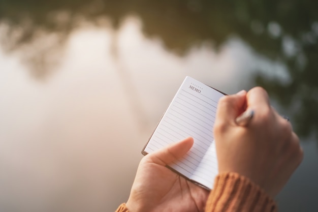 Copie el espacio de la mano de la mujer que escribe en el cuaderno blanco con el fondo de la luz del sol.