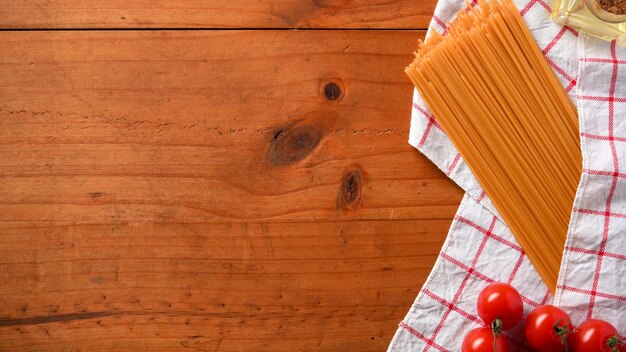 Copie el espacio sobre fondo de madera con espaguetis crudos tomates frescos y vista superior de mantel