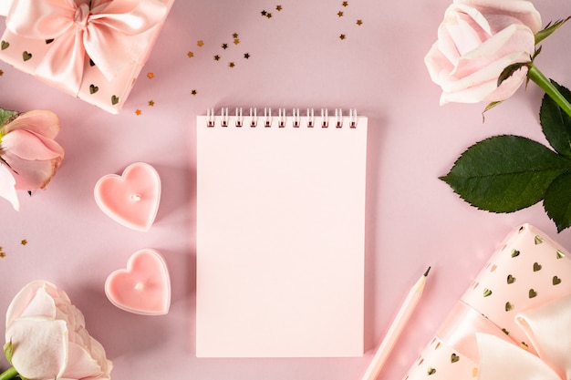 Copie o bloco de notas de espaço para o seu texto em uma mesa rosa clara com rosas cor de rosa e caixas de presente. colocação plana. Vista do topo.
