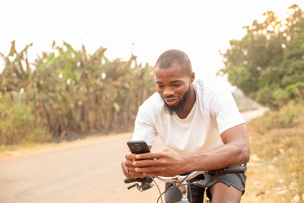 Copie o espaço do jovem negro sorrindo usando o telefone enquanto está sentado na bicicleta