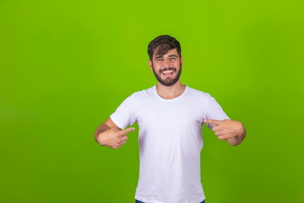 Copie o espaço em sua camiseta Retrato de um jovem alegre olhando para a câmera e apontando para o espaço de cópia em sua camiseta em pé contra um fundo verde
