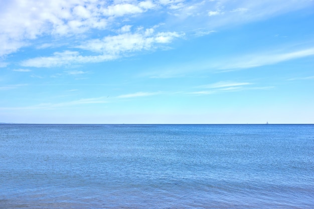 Copie o espaço no mar com um fundo de céu azul nublado Ondas calmas do oceano em uma praia vazia com um veleiro cruzando no horizonte Paisagem cênica e pitoresca para umas férias de verão tranquilas