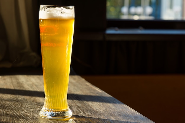 Copo alto de cerveja na mesa com o sol passando pela janela