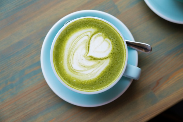 Foto copo azul com matcha latte em uma mesa de madeira.