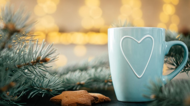 Copo azul parcialmente turva com coração em bokeh de fundo de luzes de Natal com galhos de árvores de Natal e biscoitos de gengibre. Copie o espaço.