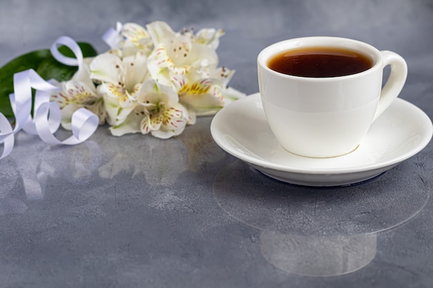 Copo branco com café em um fundo cinza. um buquê de orquídeas entrelaçadas com uma fita no fundo. banners, parabéns pelo feriado. copie o espaço.