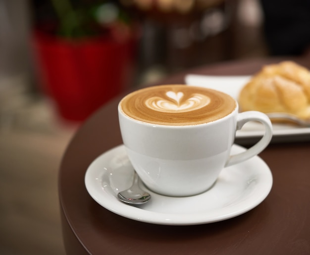 Copo branco com cappuccino em uma mesa marrom