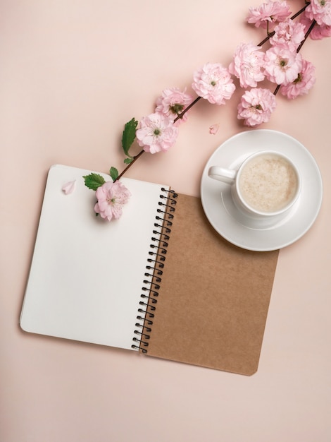 Copo branco com cappuccino, flores de sakura, caderno em um fundo do rosa pastel. dia das mães