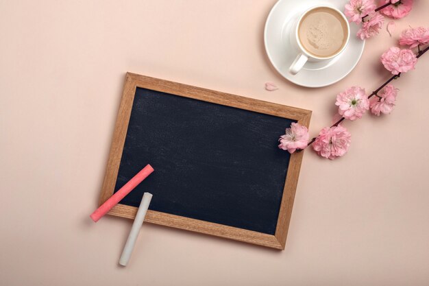 Copo branco com cappuccino, flores de sakura, quadro de giz sobre um fundo rosa pastel.