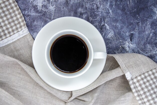 Copo branco de café preto americano e um lindo xale feito de tecido sobre uma mesa cinza. Bela composição da taça. Camada plana, vista superior, espaço de cópia. Conceito de relaxamento.