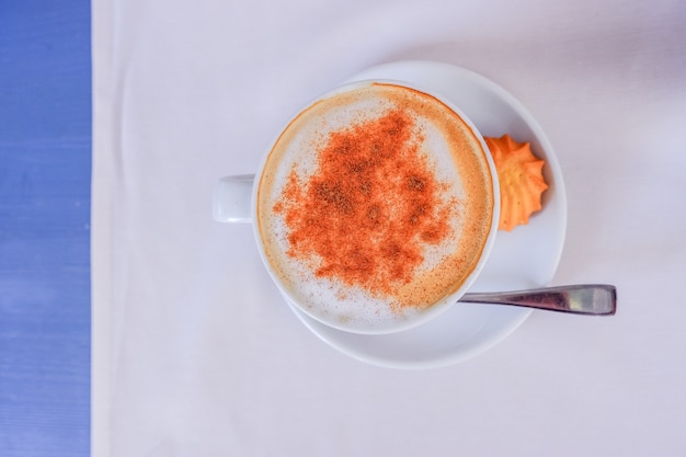 Copo branco do cappuccino com canela na luz - tabela azul com guardanapo branco, vista superior. bom dia café conceito de bebidas quentes. copie o espaço