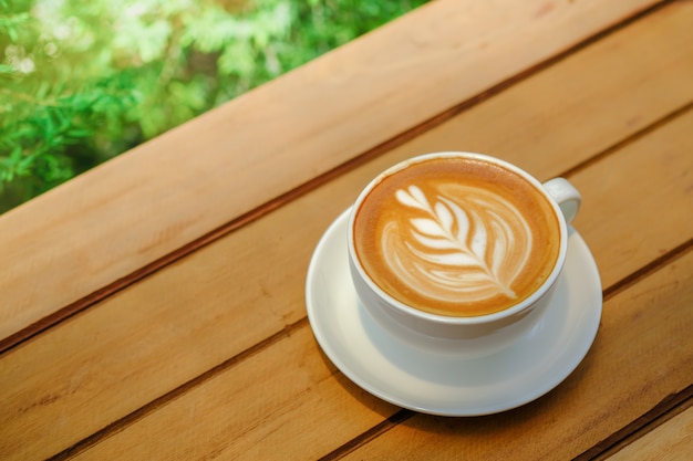 copo branco do latte quente do café com arte da forma do coração da espuma do leite com natureza verde.