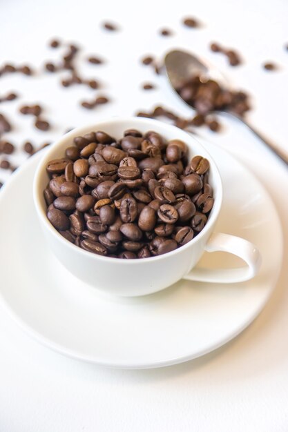 Copo branco e grãos de café em um fundo branco. Foco seletivo.