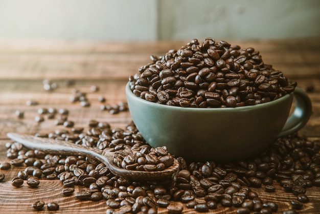 Copo cheio de grãos de café preto deita-se sobre uma mesa de madeira marrom, imagem de fundo. grãos de café em uma xícara verde.