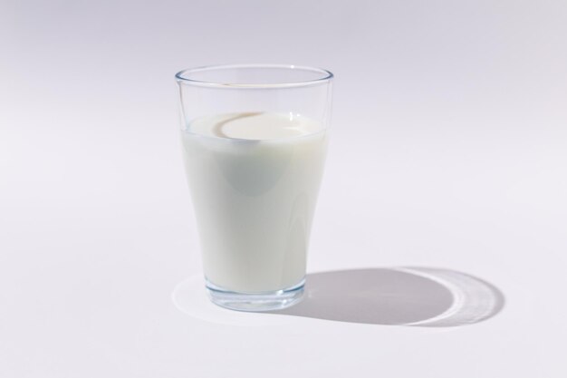 Copo cheio de leite em luz dura sobre fundo BRANCO Escassez de laticínios, crescimento e conceito de bebida