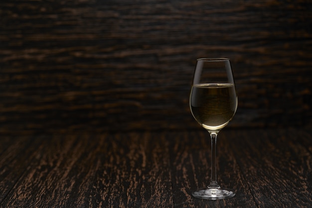 Copo cheio de vinho branco em uma mesa de madeira preta, com espaço de cópia.