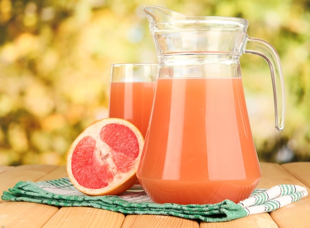 Foto copo cheio e jarro de suco de toranja e toranjas na mesa de madeira ao ar livre