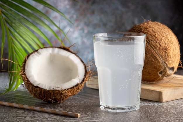 Copo com água de coco fresca e cocos em cima da mesa