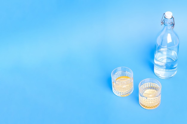 Copo com água e limão perto da garrafa no fundo azul com espaço de cópia