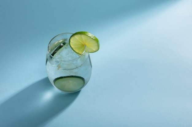 Copo com água mineral e gelo com rodelas de pepino e limão em um fundo azul