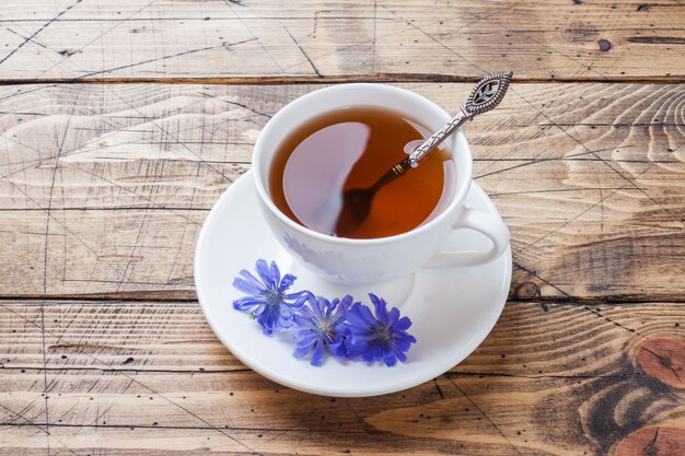 Copo com bebida de chicória e flores de chicória azul na mesa de madeira