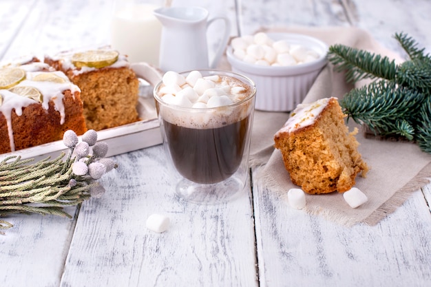 Copo com café e pequenos marshmallows, bolo de limão e galho de árvore de natal