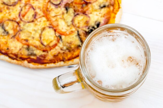 Copo com cerveja e pizza assada na mesa branca Vista superior