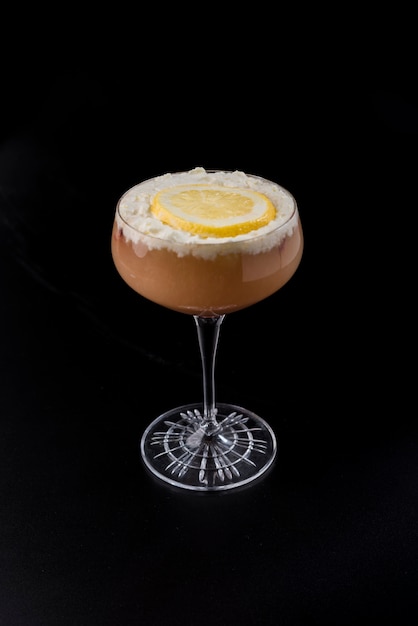 Copo com cocktail vermelho com fatia de creme e laranja em fundo preto