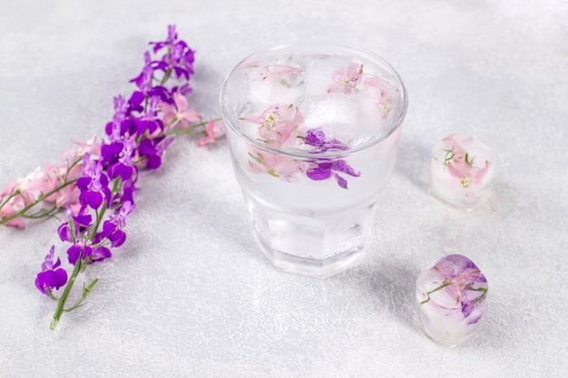 Copo com limonada e cubos de gelo com flores roxas e rosa suave.