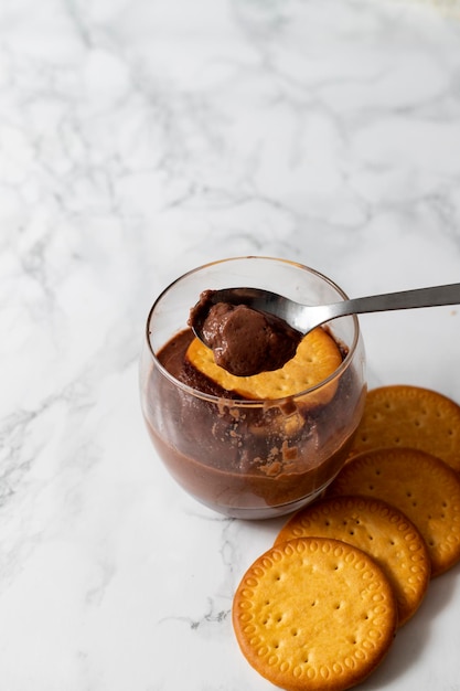 Copo com mousse de chocolate com uma colher cheia de mousse e biscoitos