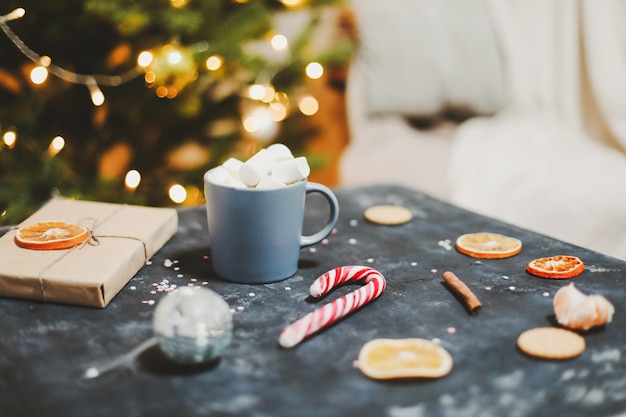 Copo com tangerinas de cana-de-doce de marshmallows por fundo de árvore de natal vida ainda de ano novo