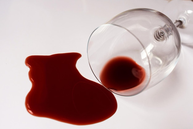 Copo com vinho tinto derramado em um fundo branco Closeup