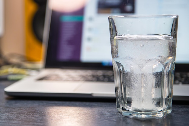 Copo de água com aspirina. laptop em segundo plano. sobrecarregado com trabalho de escritório