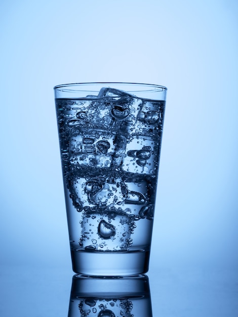 Copo de água com cubos de gelo em um fundo azul claro com reflexo