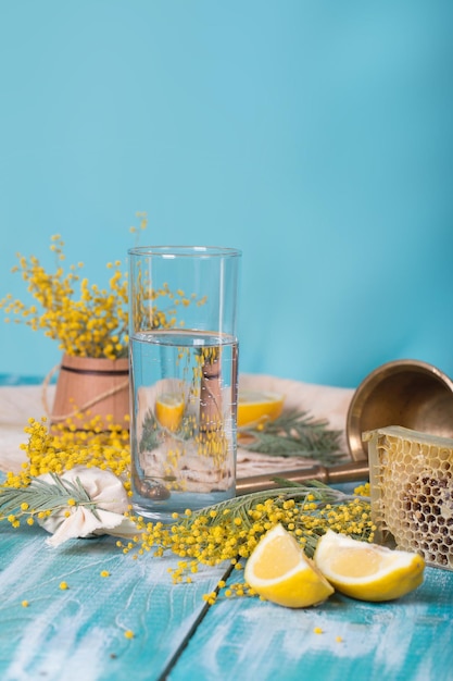 Copo de água, flores de mimosa, favo de mel e pedaços de limão sobre uma superfície de madeira. Fechar-se