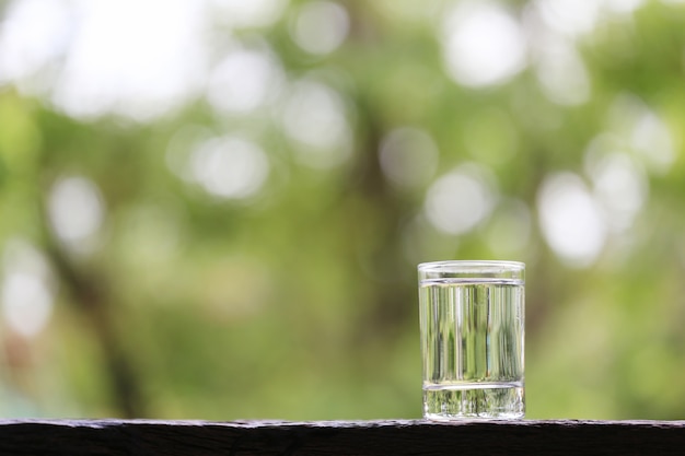 Copo de água no chão de madeira e fundo verde da natureza