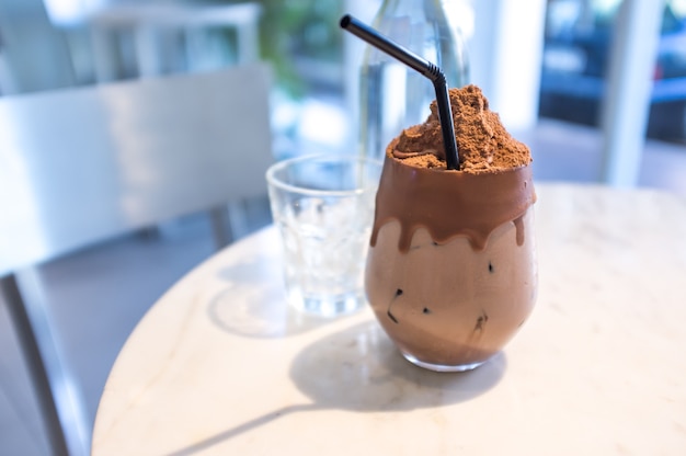 Copo de bebida de chocolate gelado com cacau em pó na mesa com copo e garrafa de água