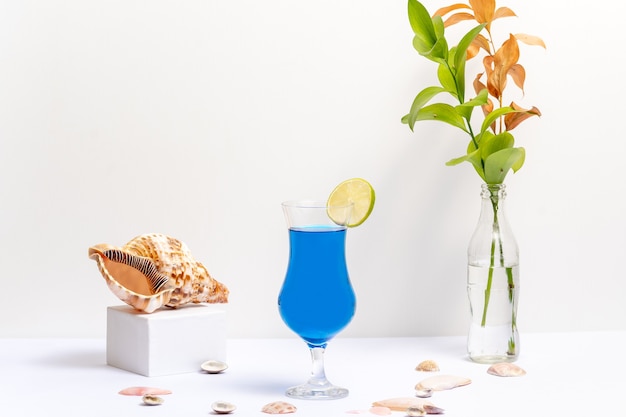 Copo de bebida de lagoa azul, em fundo branco com conchas ao lado do copo