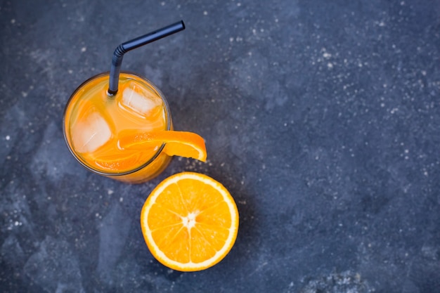 Copo de bebida de laranja com gelo sobre um fundo cinza escuro